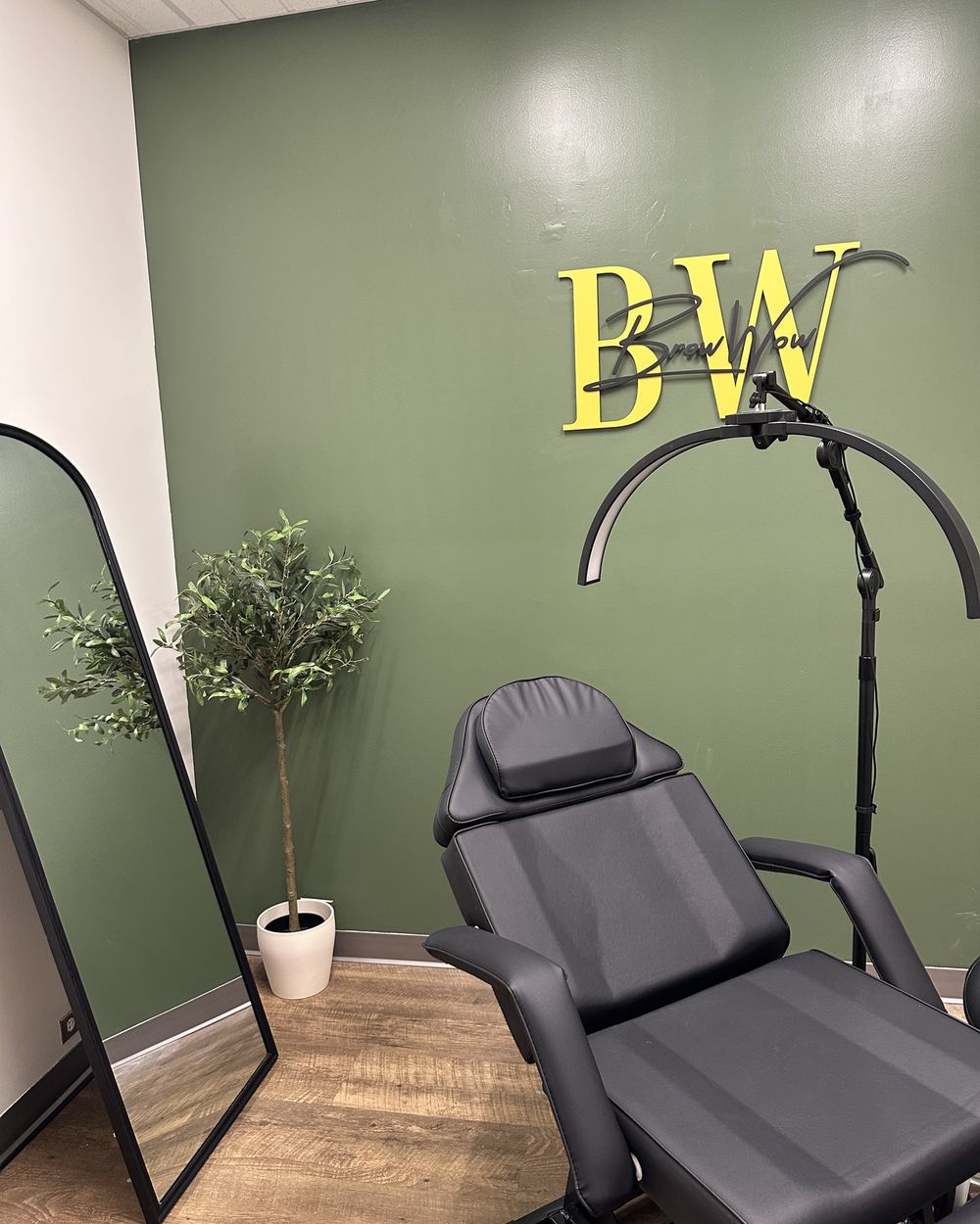 The BrowWow studio in Tempe: Laurel Garland green accent wall with the BrowWow sign, treatment chair and brow lamp